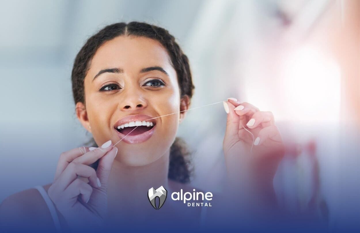 Woman flossing her teeth in front of a mirror.