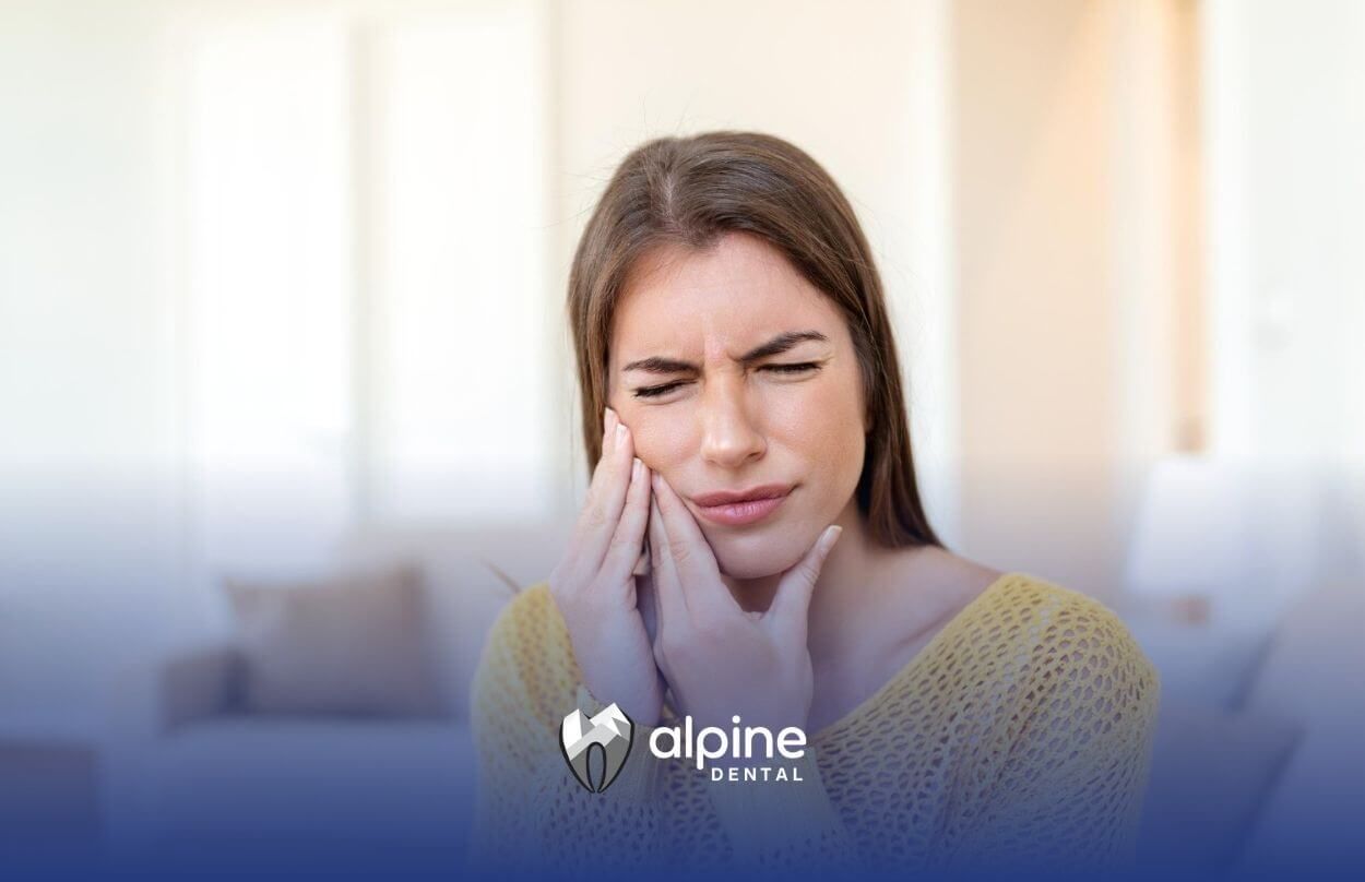 Woman in yellow sweater with eyes closed, holding her cheek in pain.
