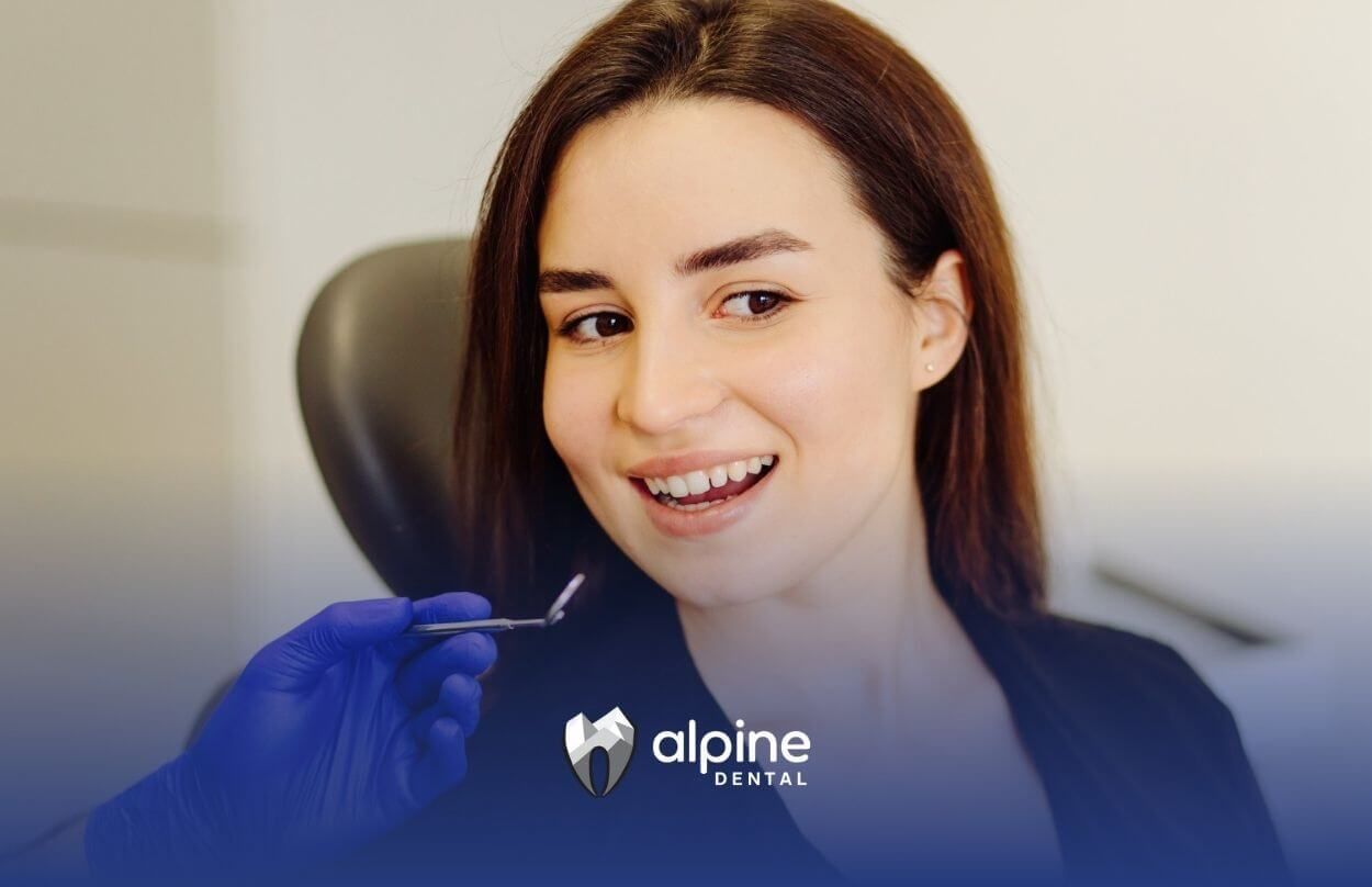 Woman smiling during a dental check-up with dentist’s hand holding a tool.
