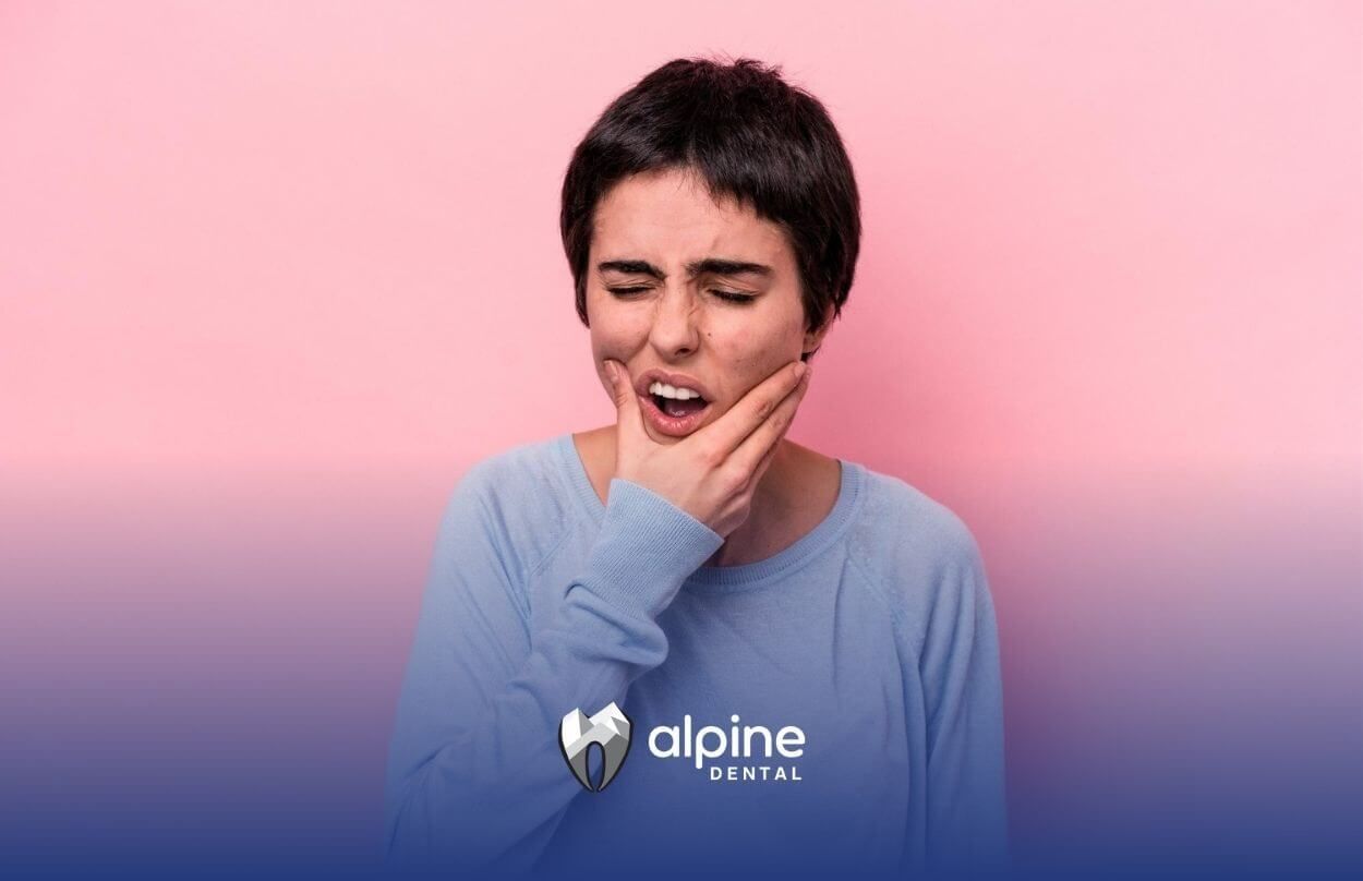 Woman holding her jaw, showing pain. Pink background.