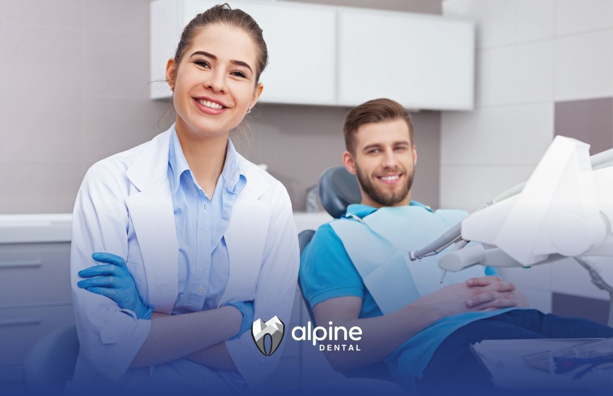 A female dentist is standing next to a man in a dental chair.