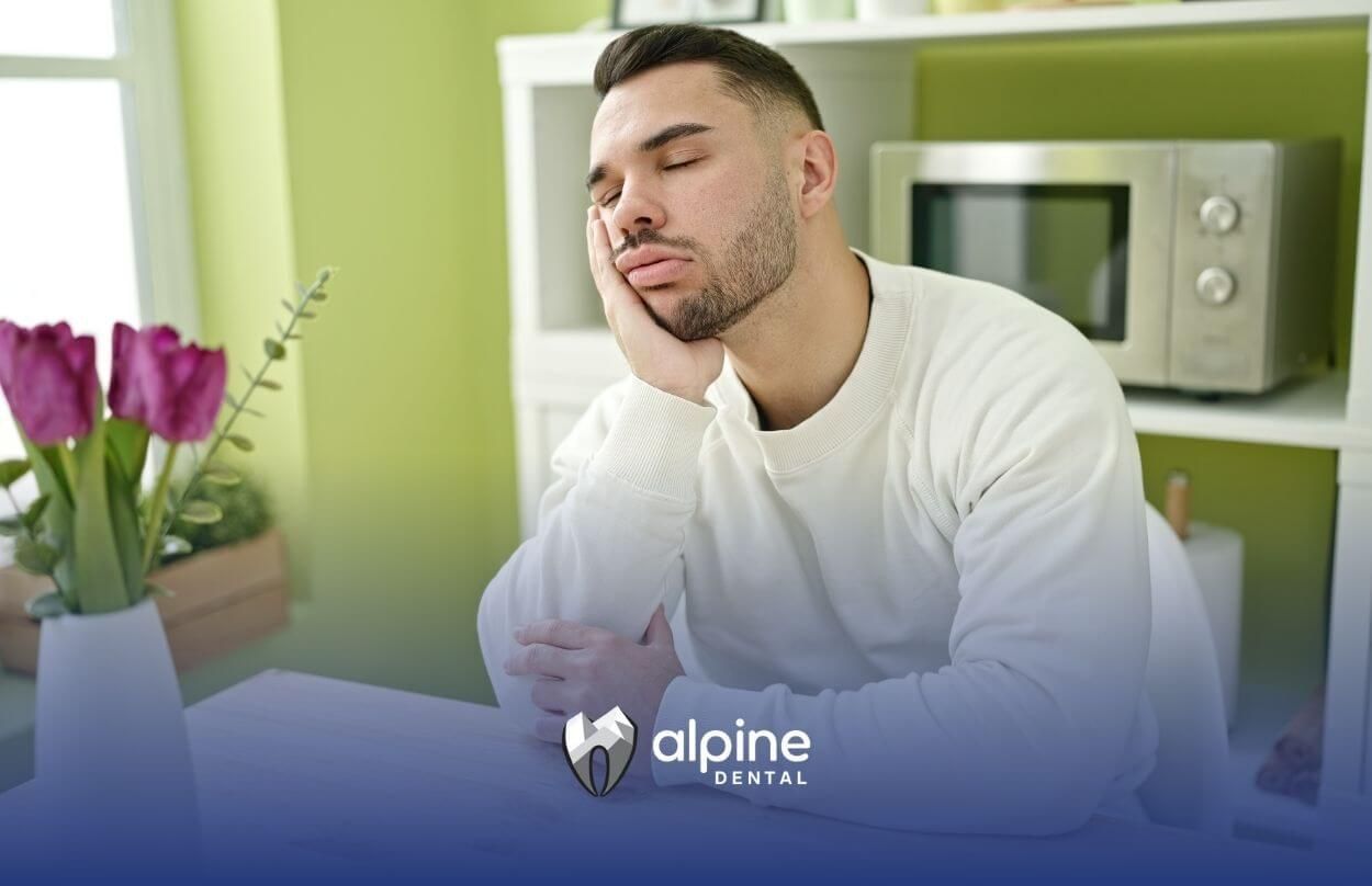 Man sitting at a table with his head resting on his hand, appearing tired or sleepy.