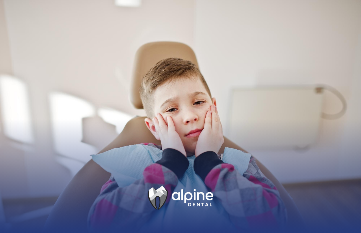 A 7-year-old boy is sitting in a dental chair with his hands on his face because of a toothache