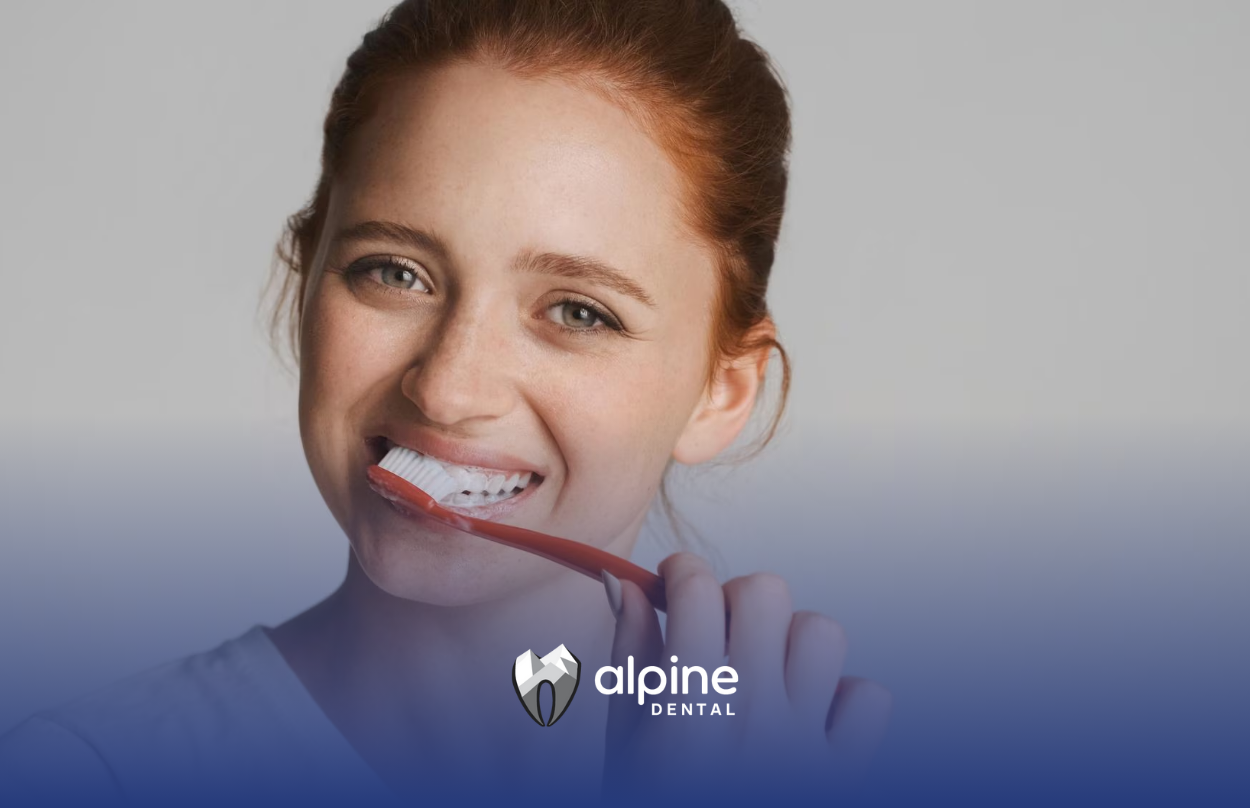 A woman is brushing her teeth with a red toothbrush.