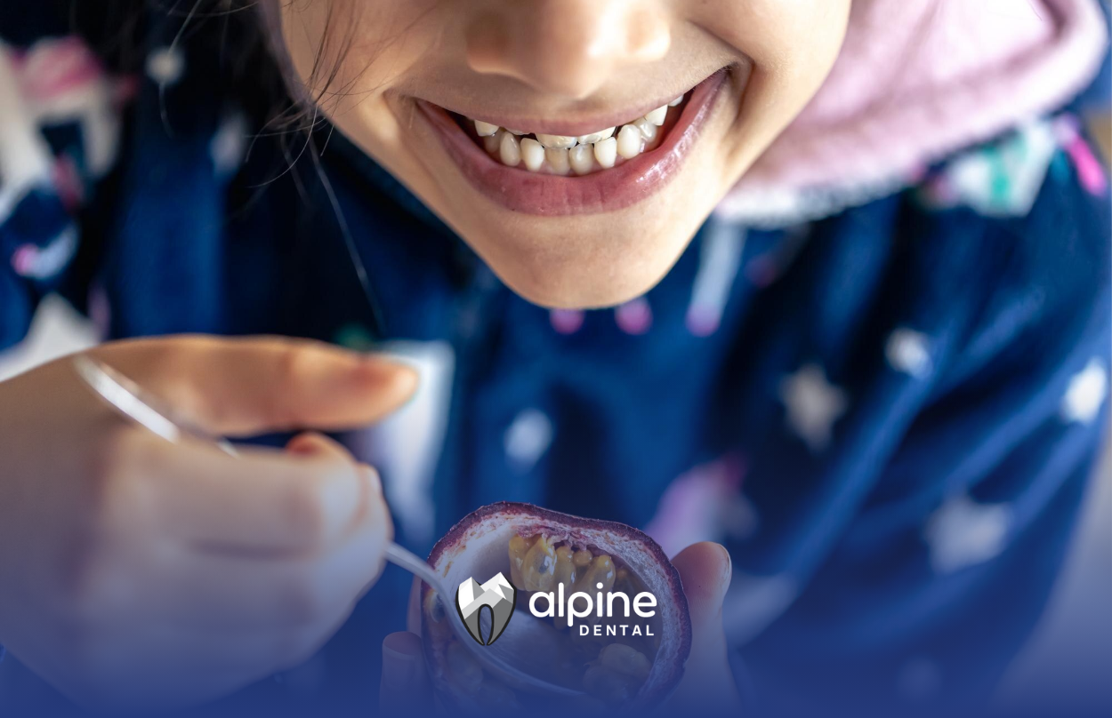 A young girl is smiling and eating fruit with a spoon.