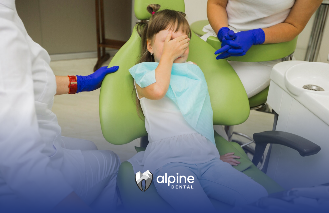 A little boy is covering his face while sitting in a dental chair.