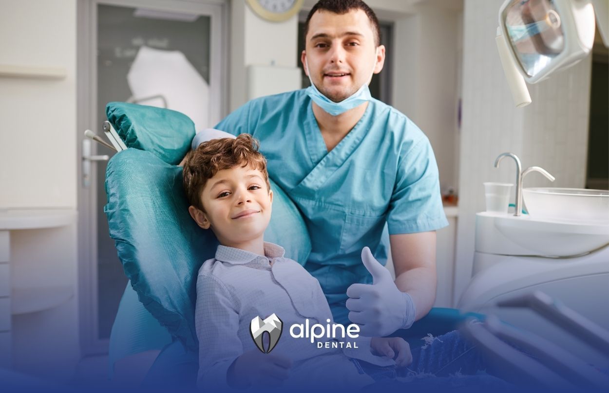 A young boy is sitting in a dental chair next to a dentist.