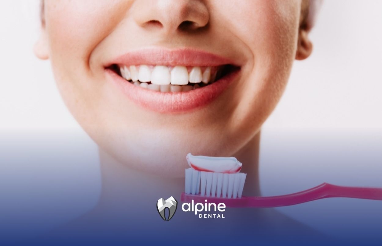 Smiling woman holding a red toothbrush with toothpaste close to her mouth after dental visit in NJ.