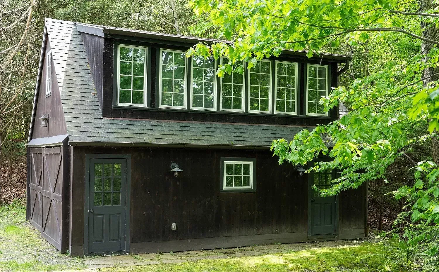 A large wooden barn with lots of windows is surrounded by trees.
