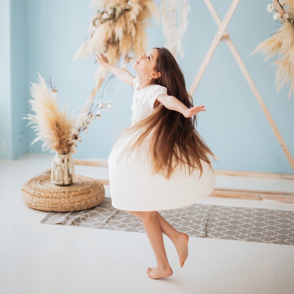 A little girl in a white dress is dancing in a room.