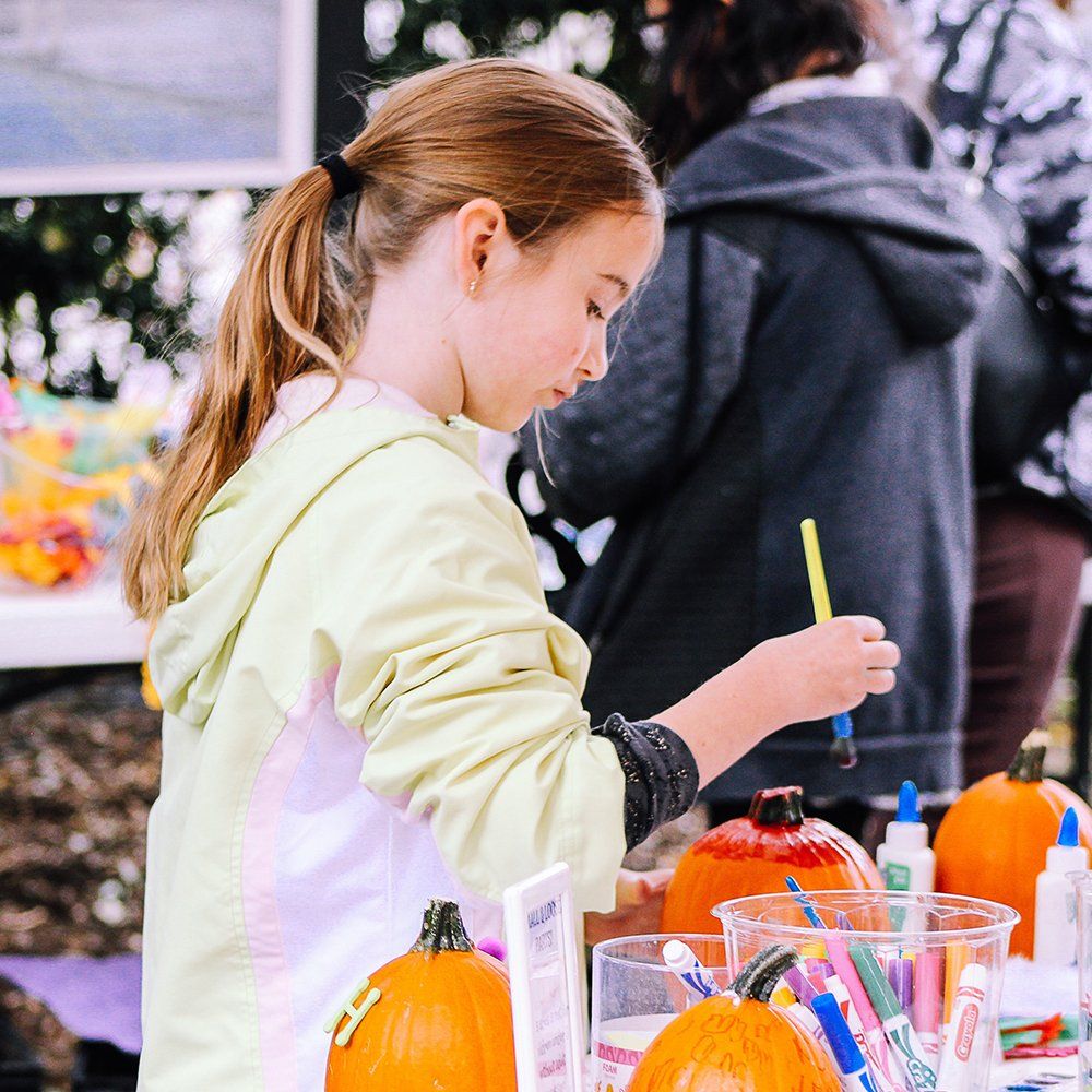 A young girl is painting a pumpkin with markers.