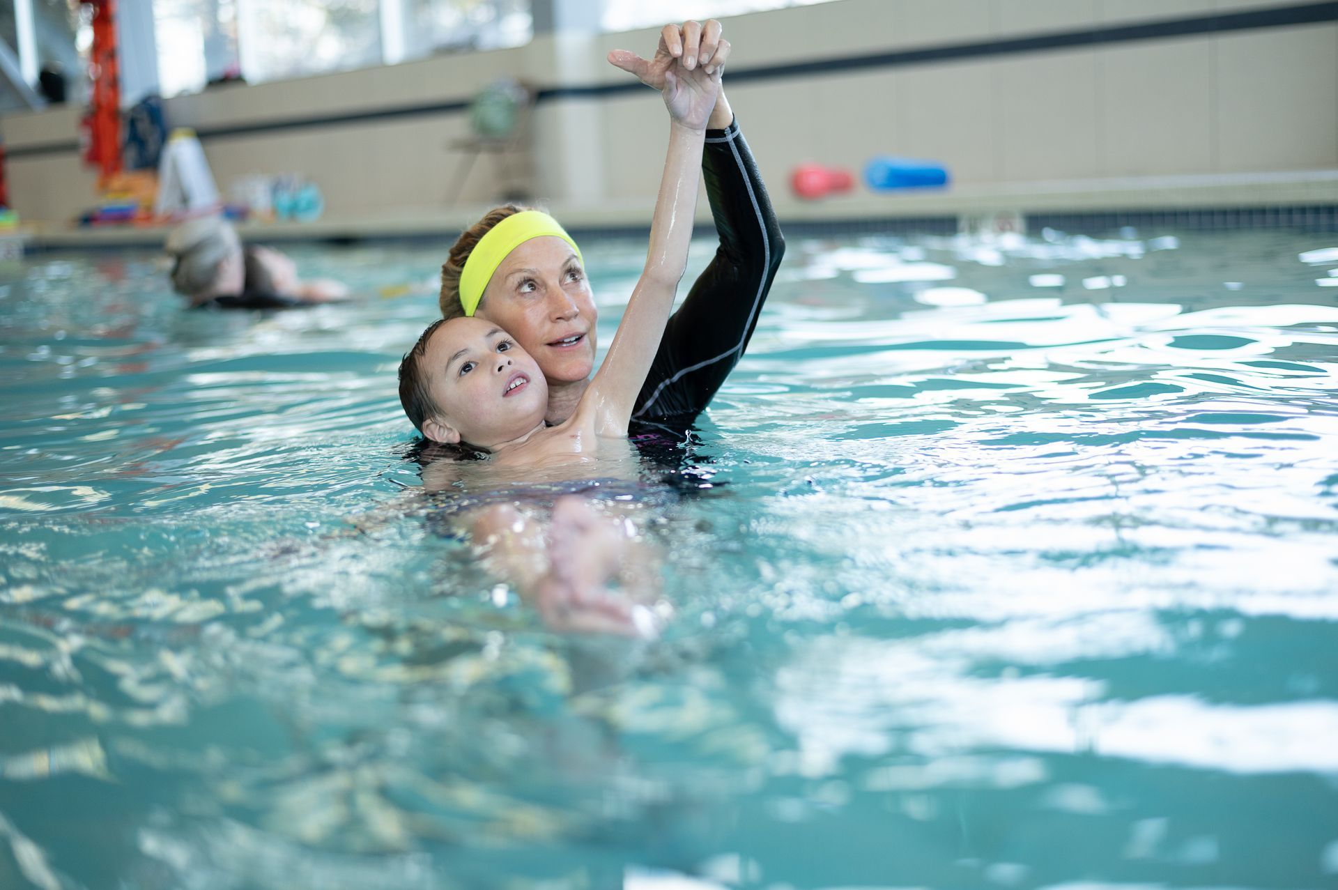 A woman is teaching a child how to swim in a swimming pool.