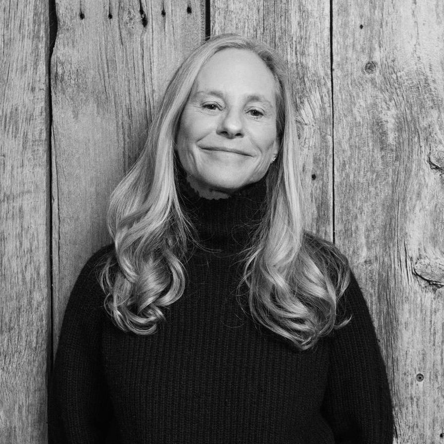 A woman in a black sweater is standing in front of a wooden wall.