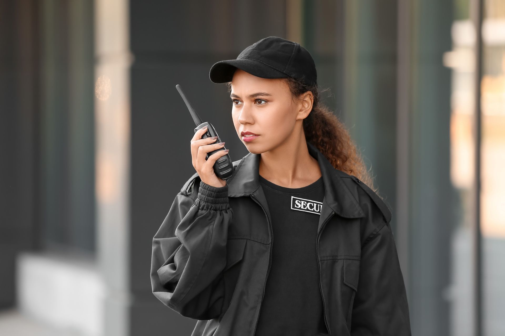 A woman in a black jacket and hat is talking on a walkie talkie.
