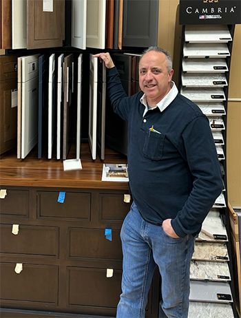 A man in a blue shirt is standing in front of a cabinet.