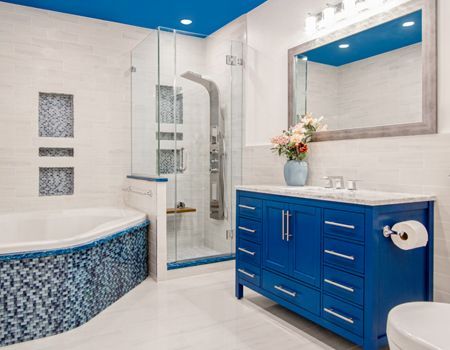 A bathroom with a blue vanity , sink , toilet and shower.