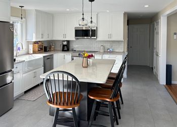 A kitchen with white cabinets , stainless steel appliances , a large island with a table and chairs.