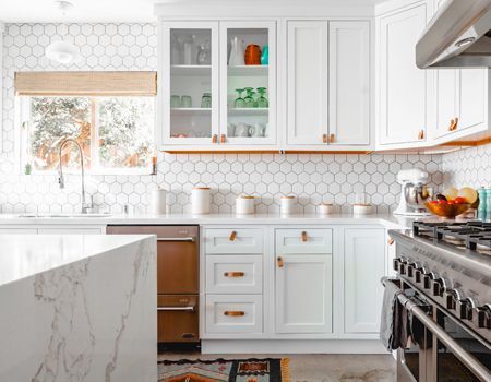 A kitchen with white cabinets , a stove , a sink , and a window.