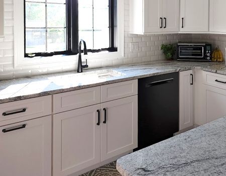 A kitchen with white cabinets , granite counter tops , and a black dishwasher.