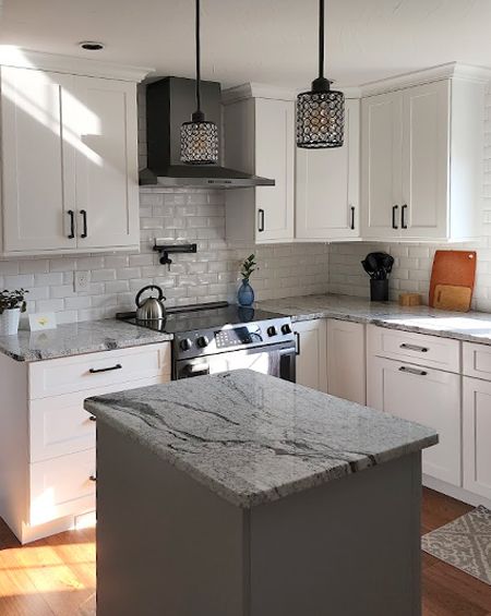 A kitchen with white cabinets , granite counter tops , a stove and a large island.