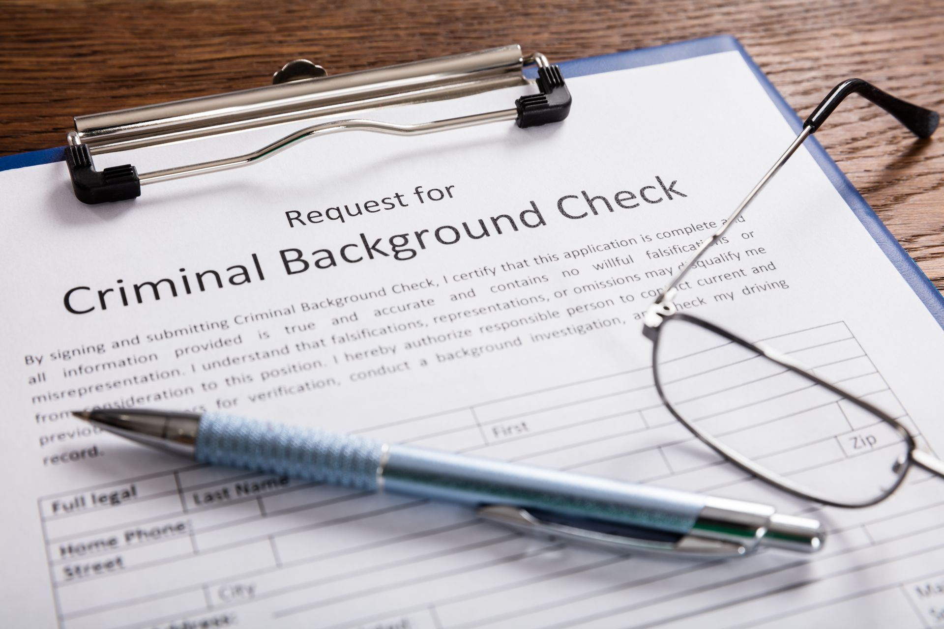 A pen and glasses are sitting on top of a criminal background check form.