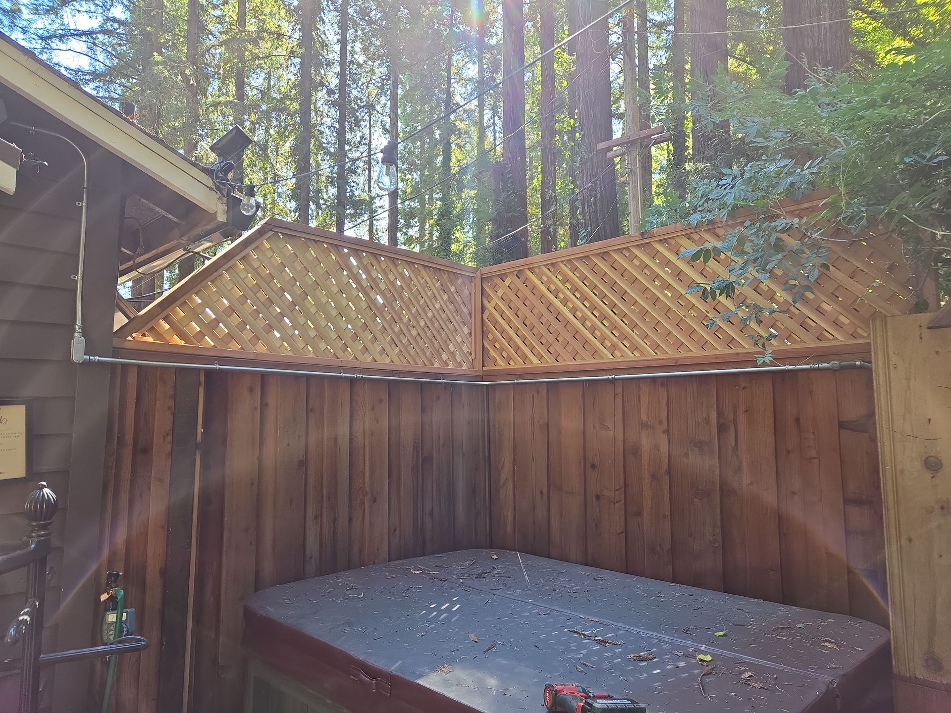 A wooden fence surrounds a hot tub in the woods.