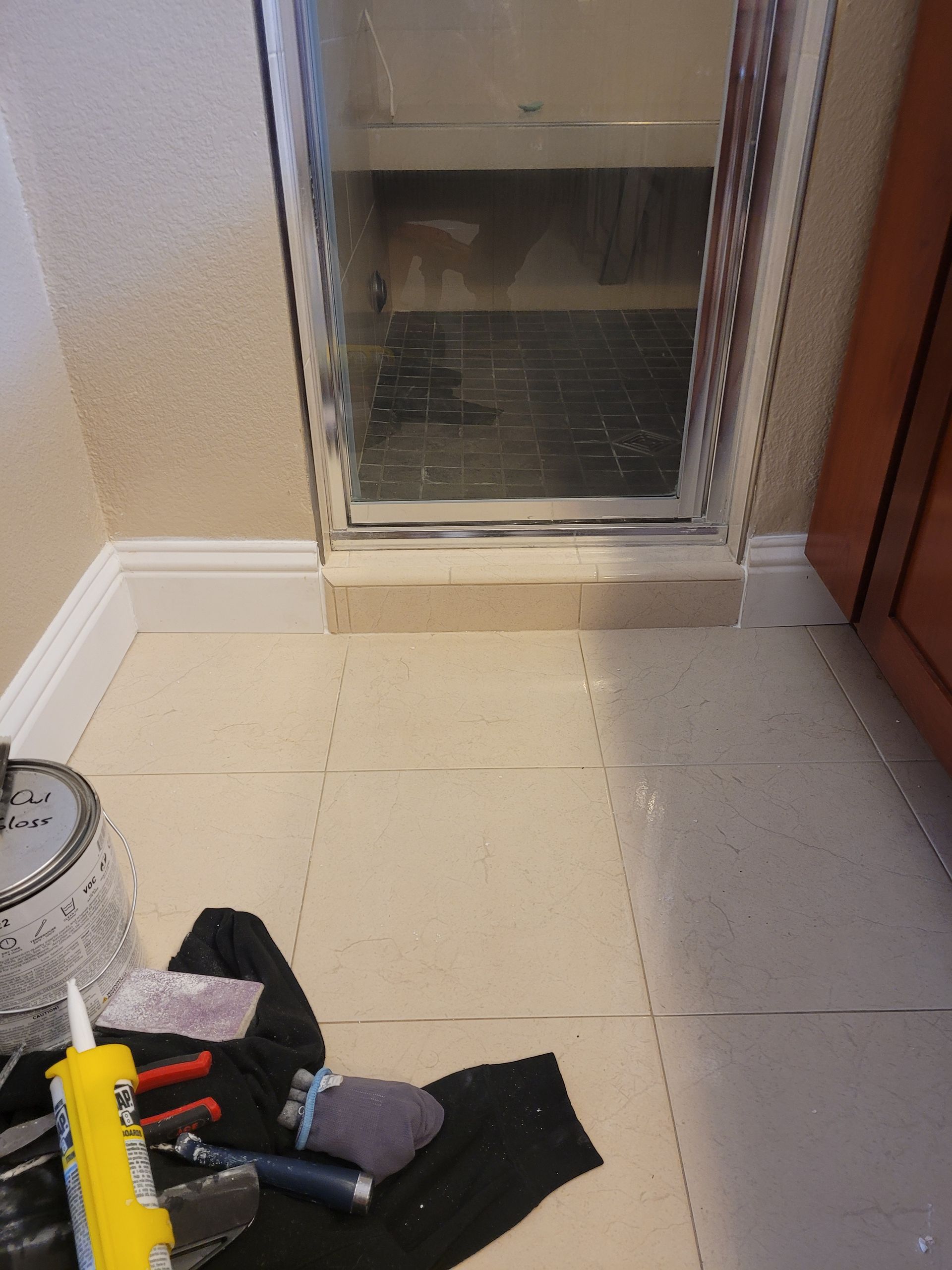 A bathroom with a shower door and tools on the floor