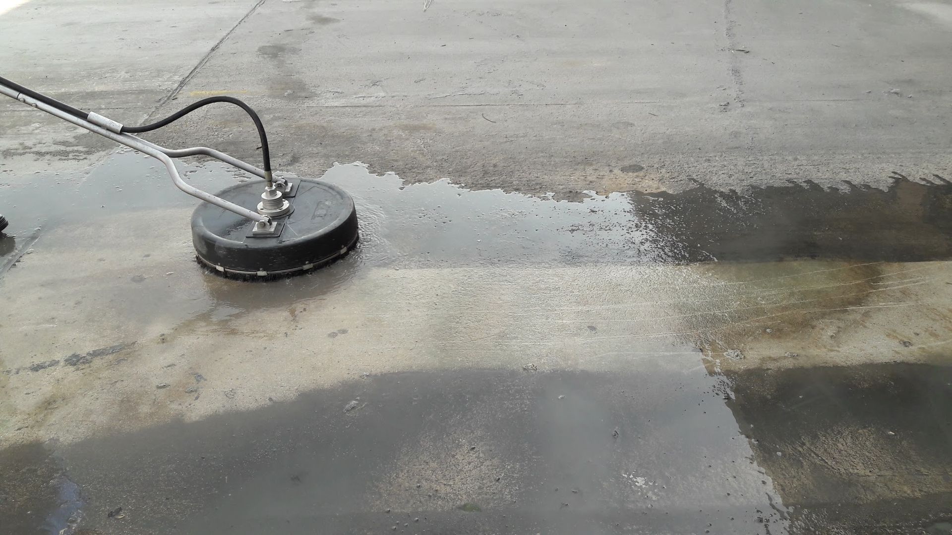 A surface cleaner is being used to clean a concrete surface, removing dirt and grime.