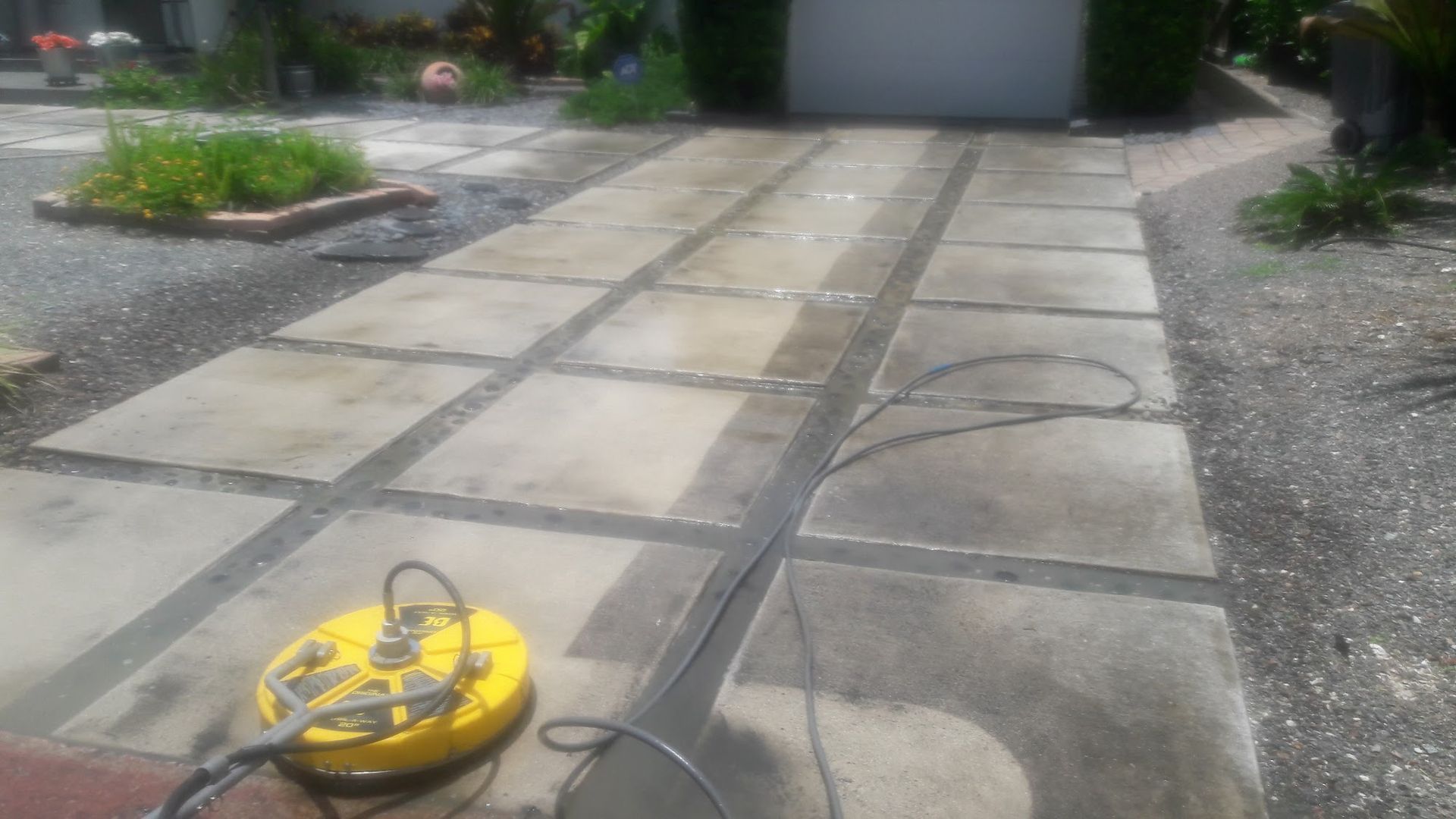 Pressure washer cleaning a concrete driveway with square pavers.