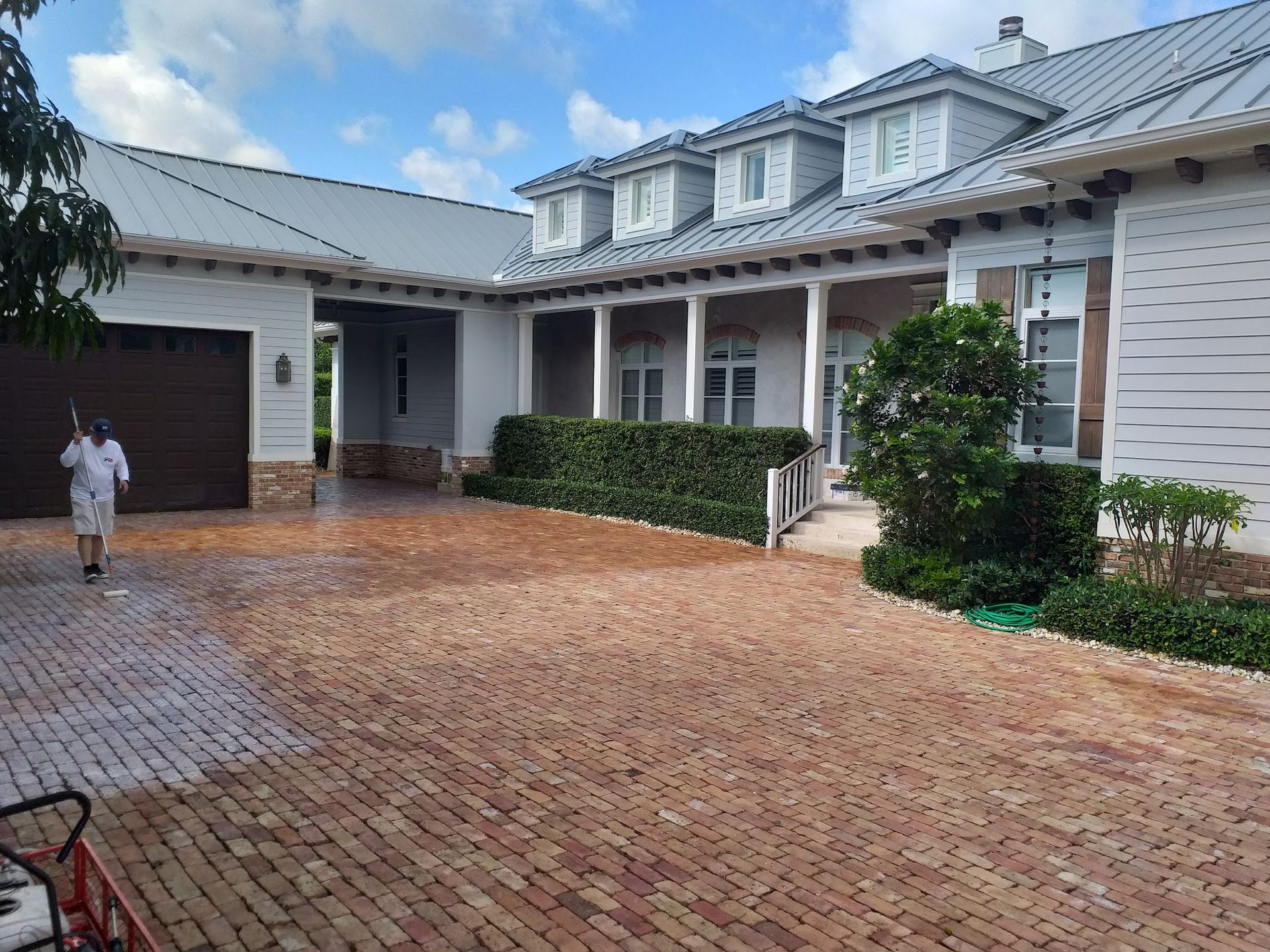 Man power washing brick driveway of a large house with blue roof.