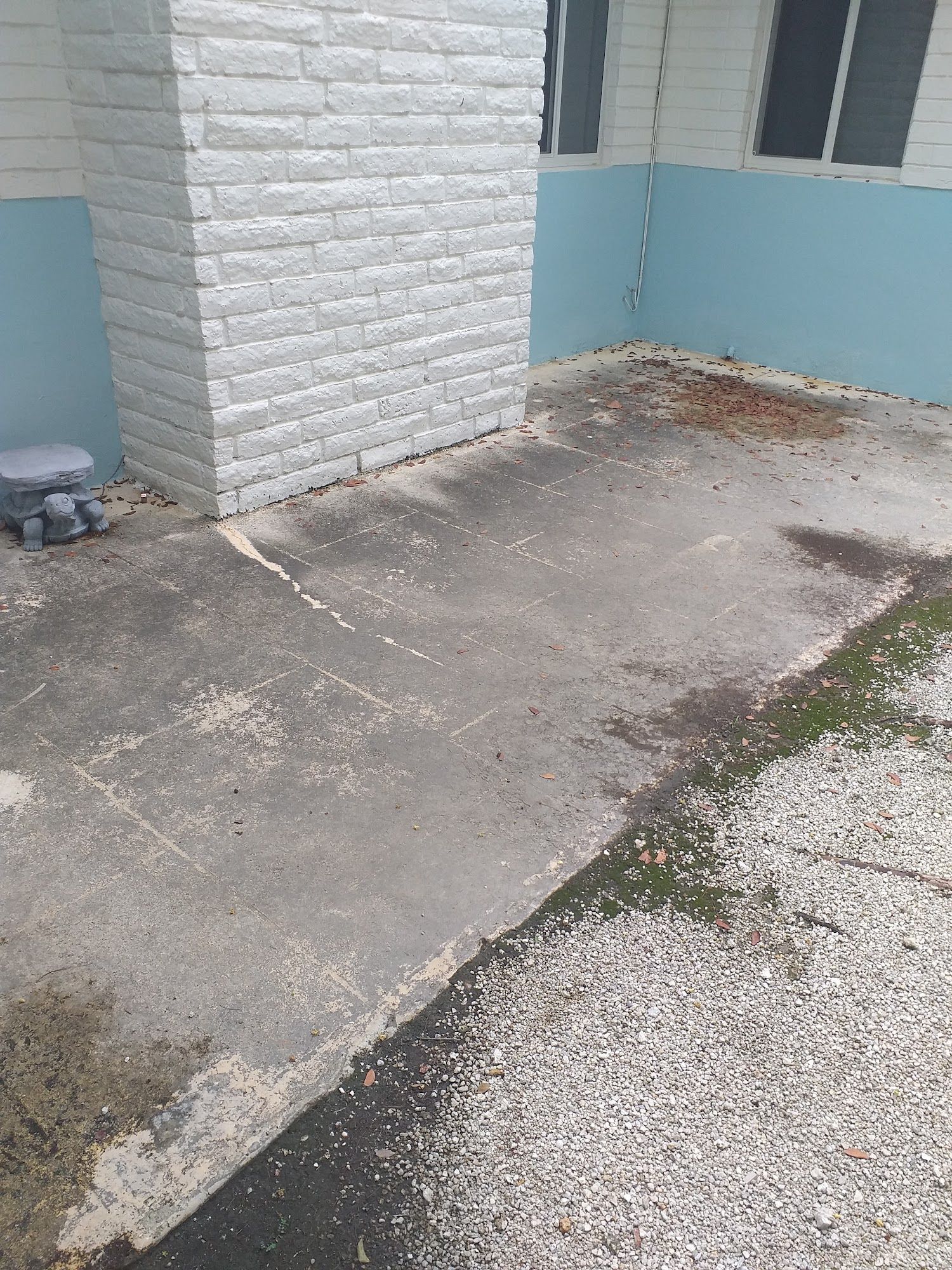 Concrete patio with moss, pebbles, and a white brick pillar against a blue-walled building.
