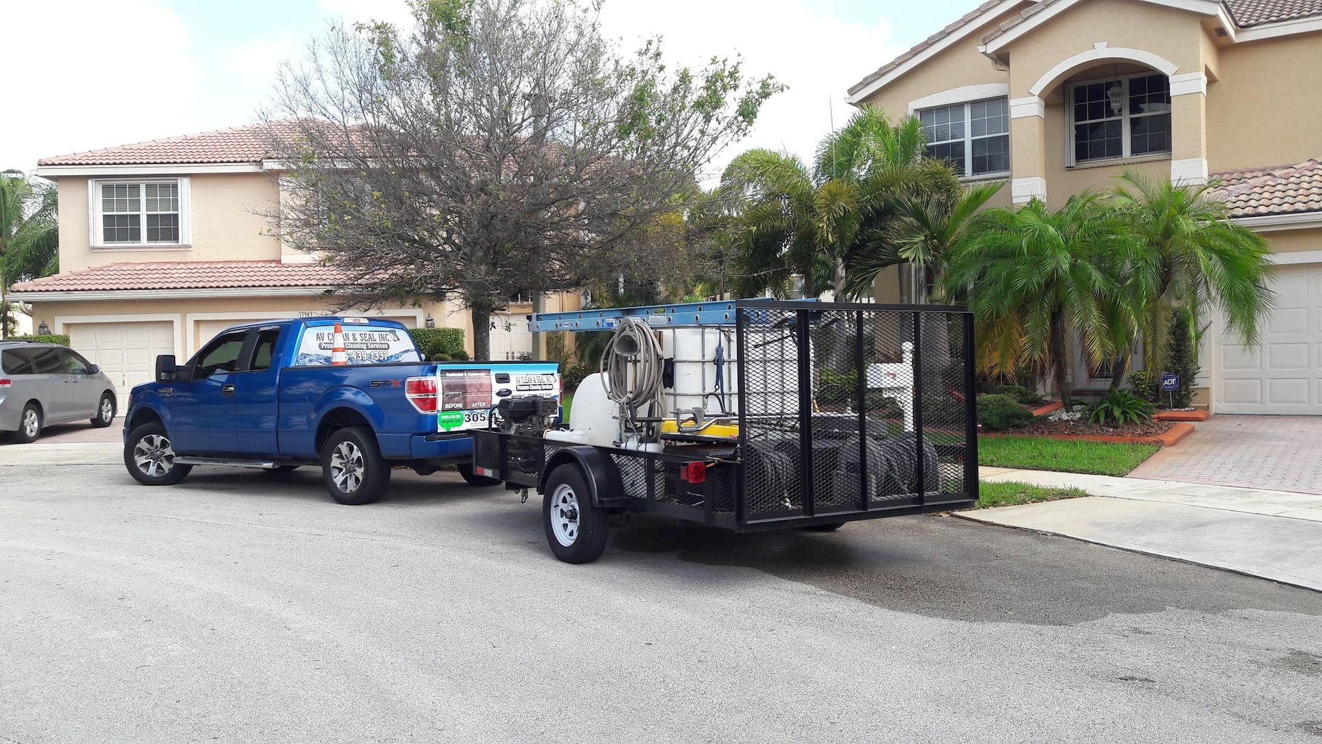 Blue truck towing a utility trailer in front of houses, likely for landscaping or maintenance.