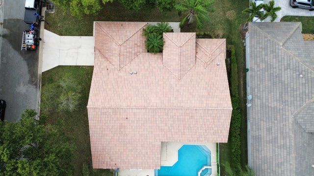 Overhead view of a house with a clay tile roof, driveway, and swimming pool.
