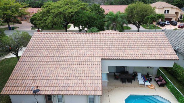 Aerial view of a house with a clay tile roof, pool, and patio with furniture.