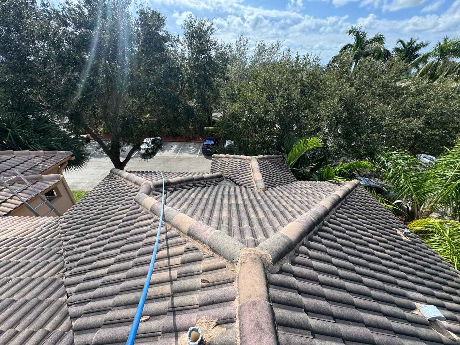View of a tiled roof from above, with trees and a street in the background on a sunny day.