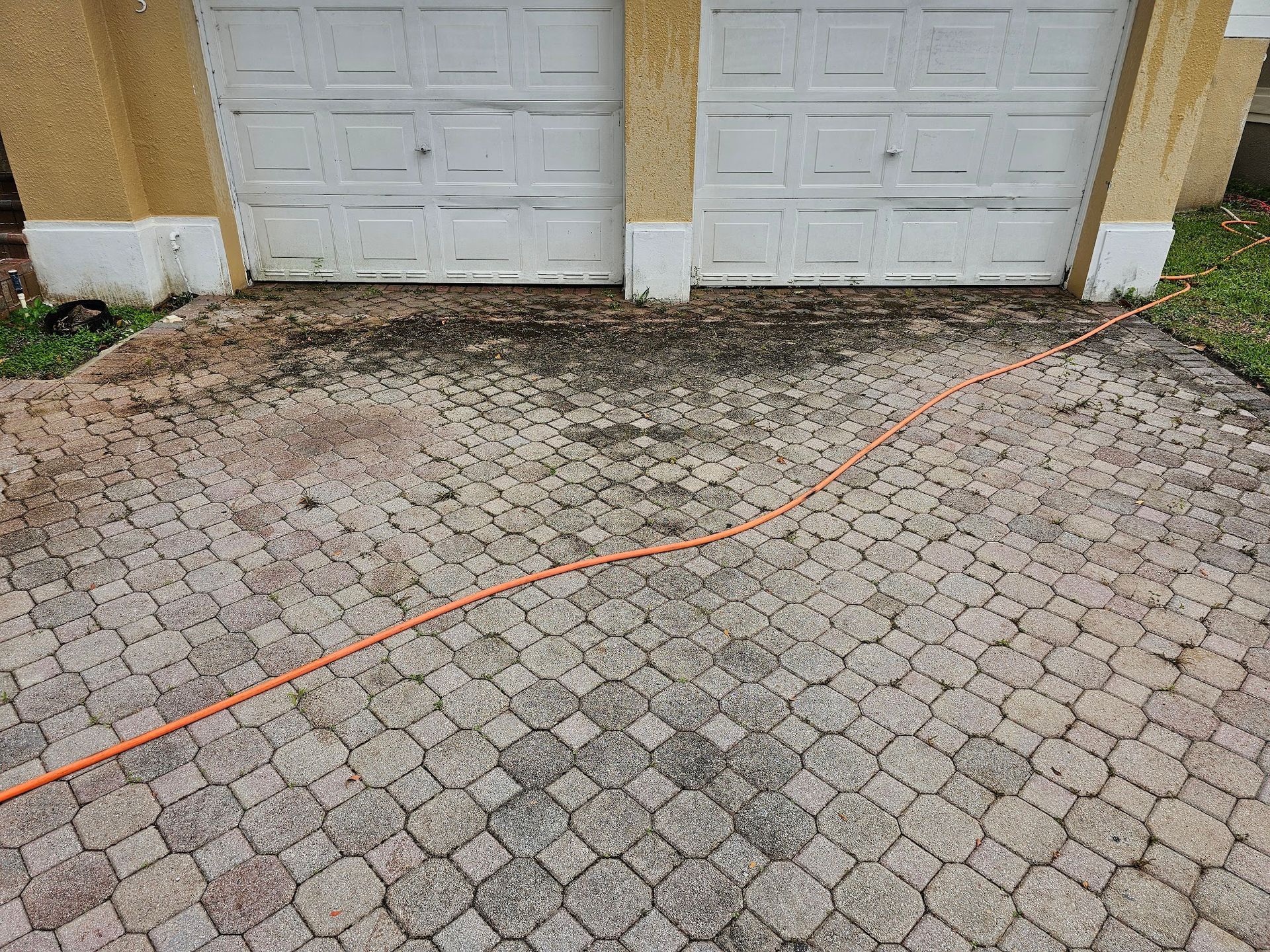 Driveway with patterned pavers and an orange hose leading to garage doors.