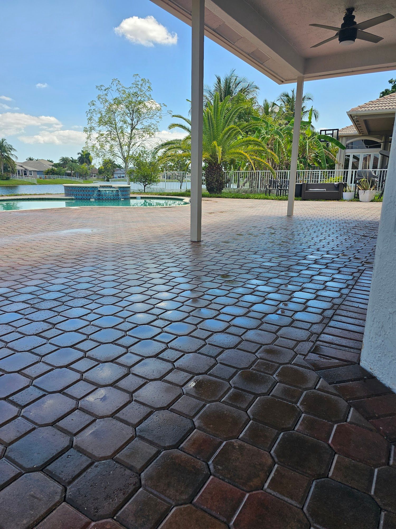 Patio with patterned brick floor, overlooking pool and lake on a sunny day.