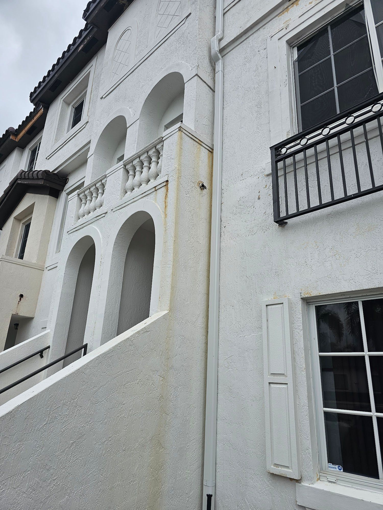 A stucco building with arched entryways, a staircase, and black railing, with light-colored walls.