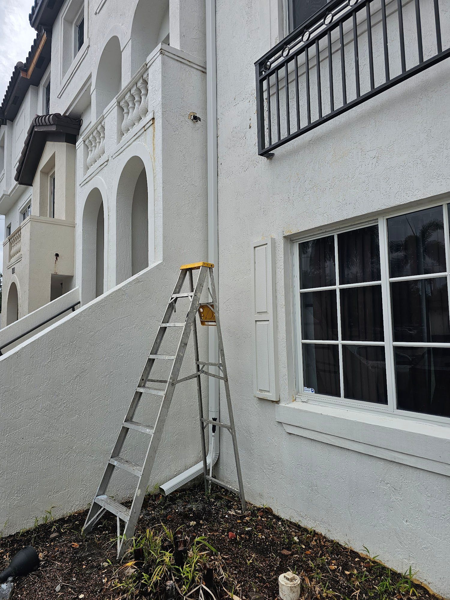 Ladder against a stucco building with a white facade. A downspout is visible.