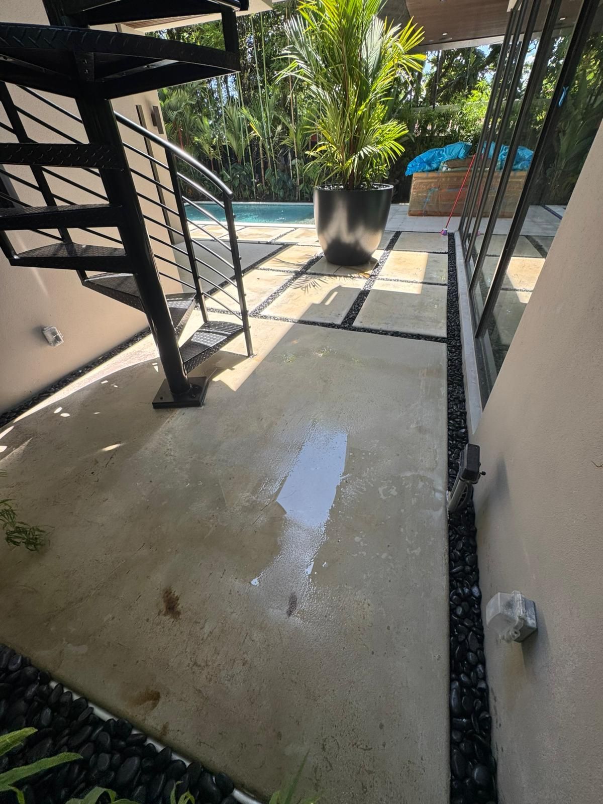 Concrete patio area with a spiral staircase and a swimming pool in the background. A light colored spill on the ground.