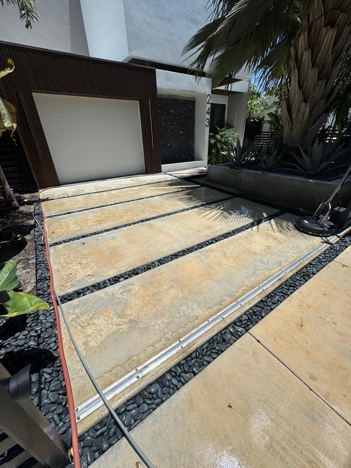 Driveway with concrete slabs and black gravel. Garage and tropical plants visible.