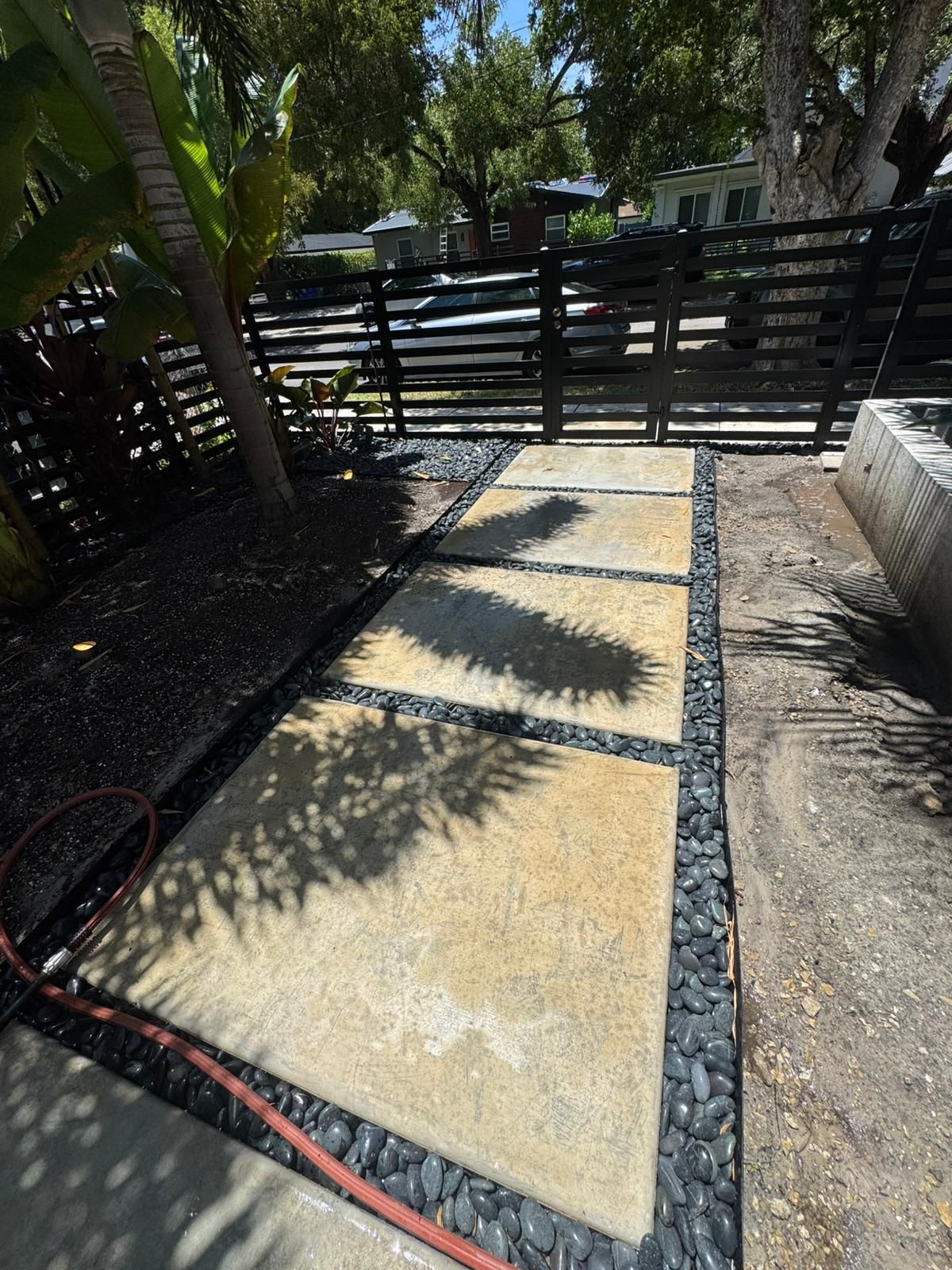 Concrete stepping stones in a yard, edged with black pebbles, near a wooden fence.