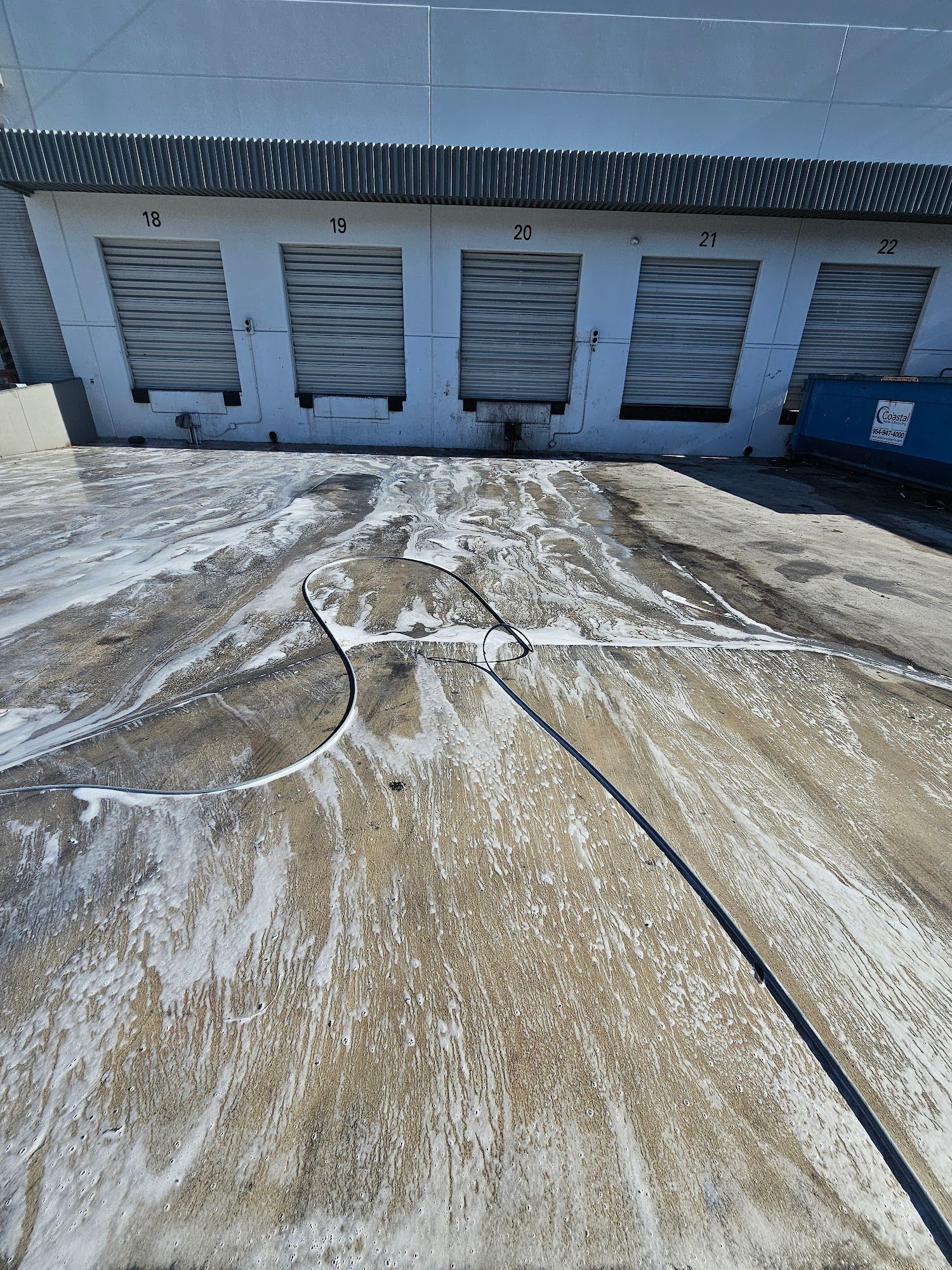 Exterior view of a concrete surface being cleaned with suds in front of warehouse doors.