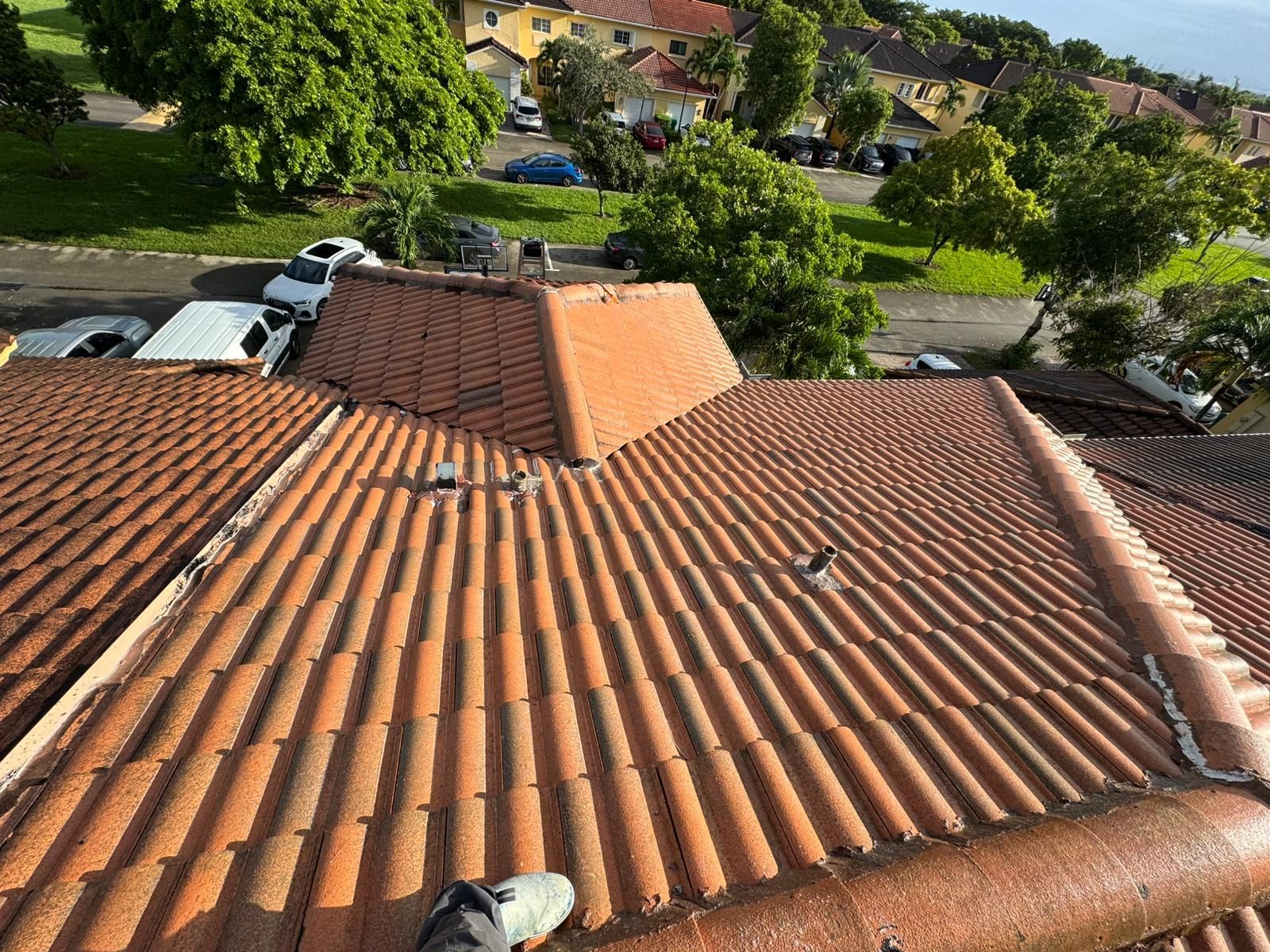 Red tiled roof of a building with a central raised section, viewed from above; a foot is visible.