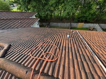 View of a red corrugated roof with an orange hose, tree line, and a white fence in the distance.