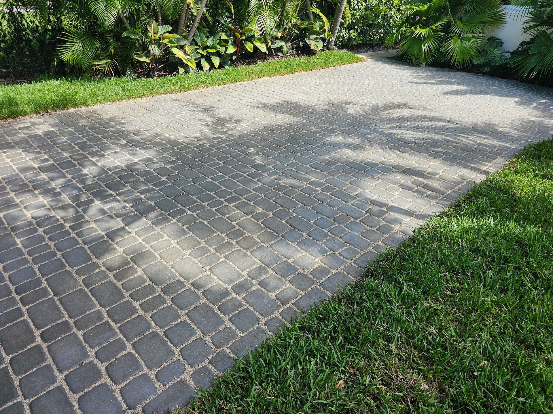 Brick paved driveway with green grass border, shaded by tree.