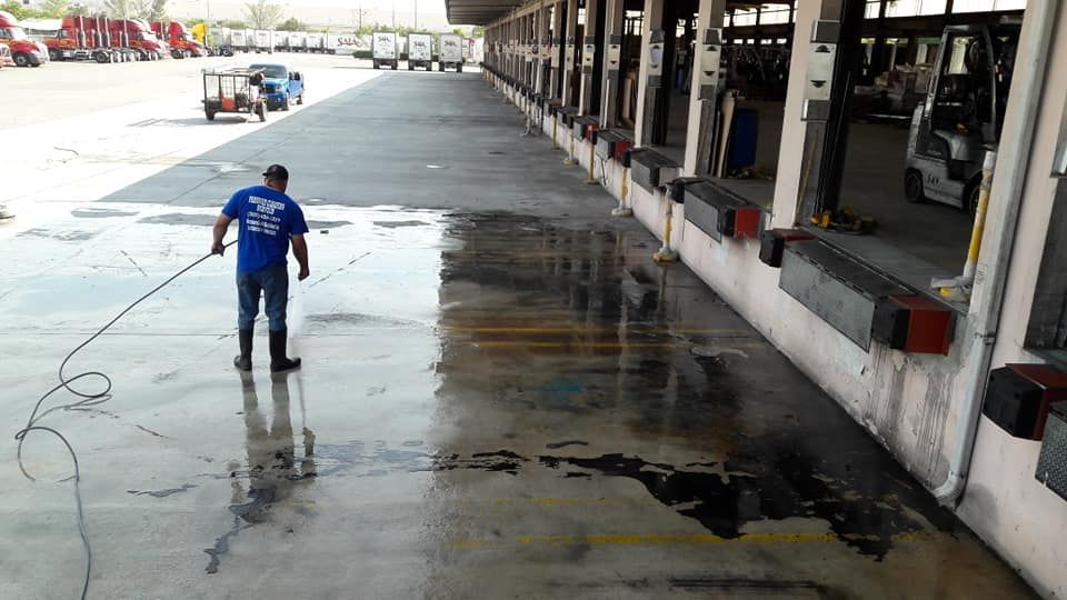 Person spraying water on a gas station concrete floor near a pump at night.