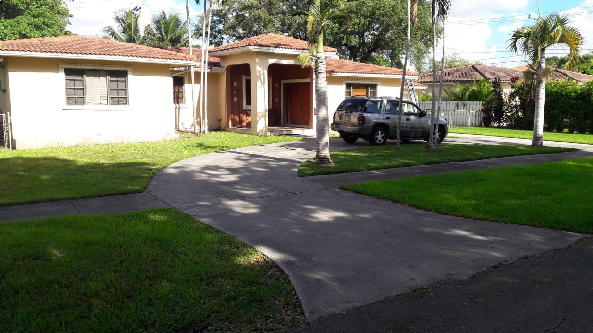 A single-story house with a driveway and a parked SUV, surrounded by green lawns.