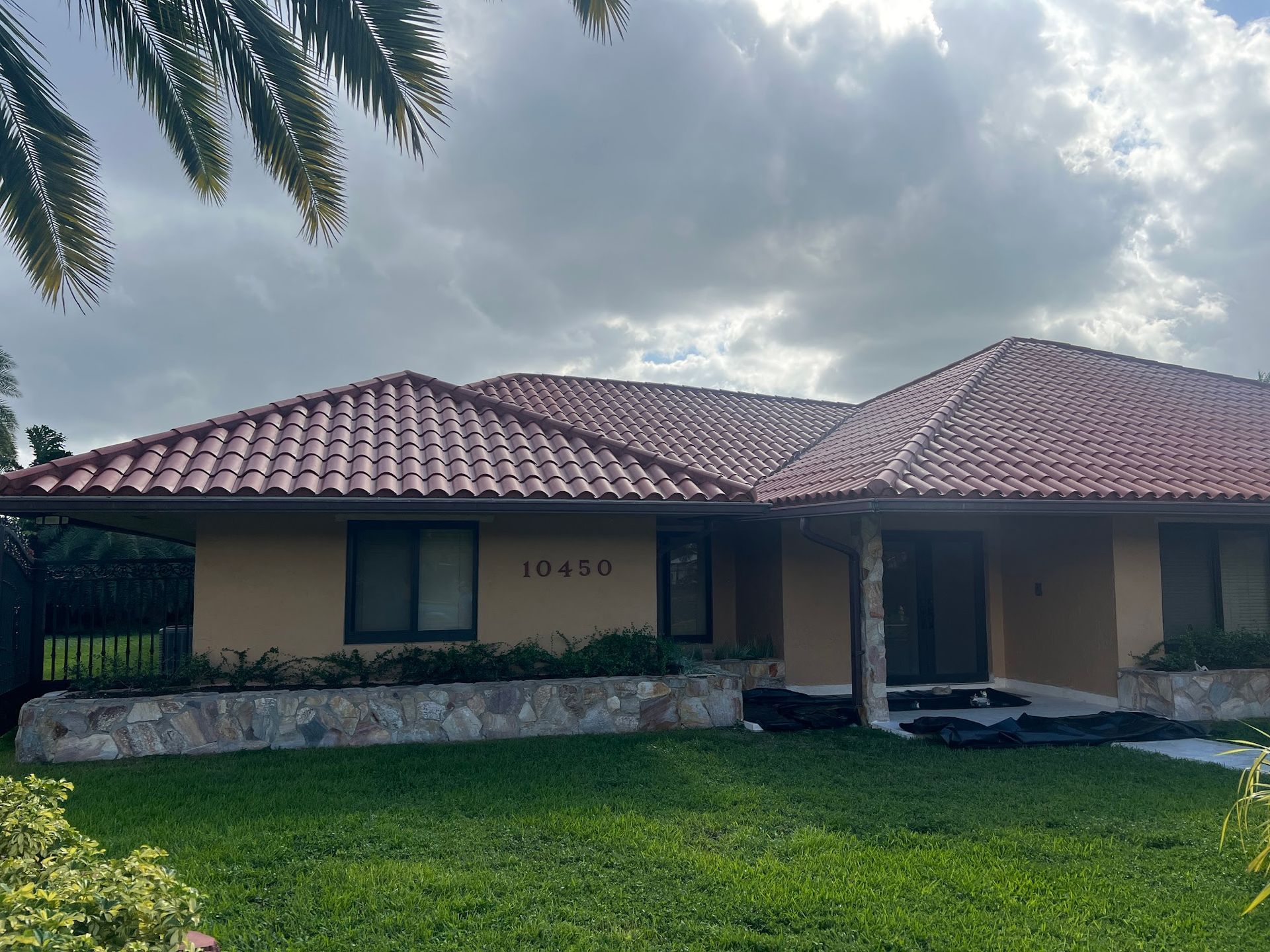 Tan house with a red tile roof, green lawn, and cloudy sky.