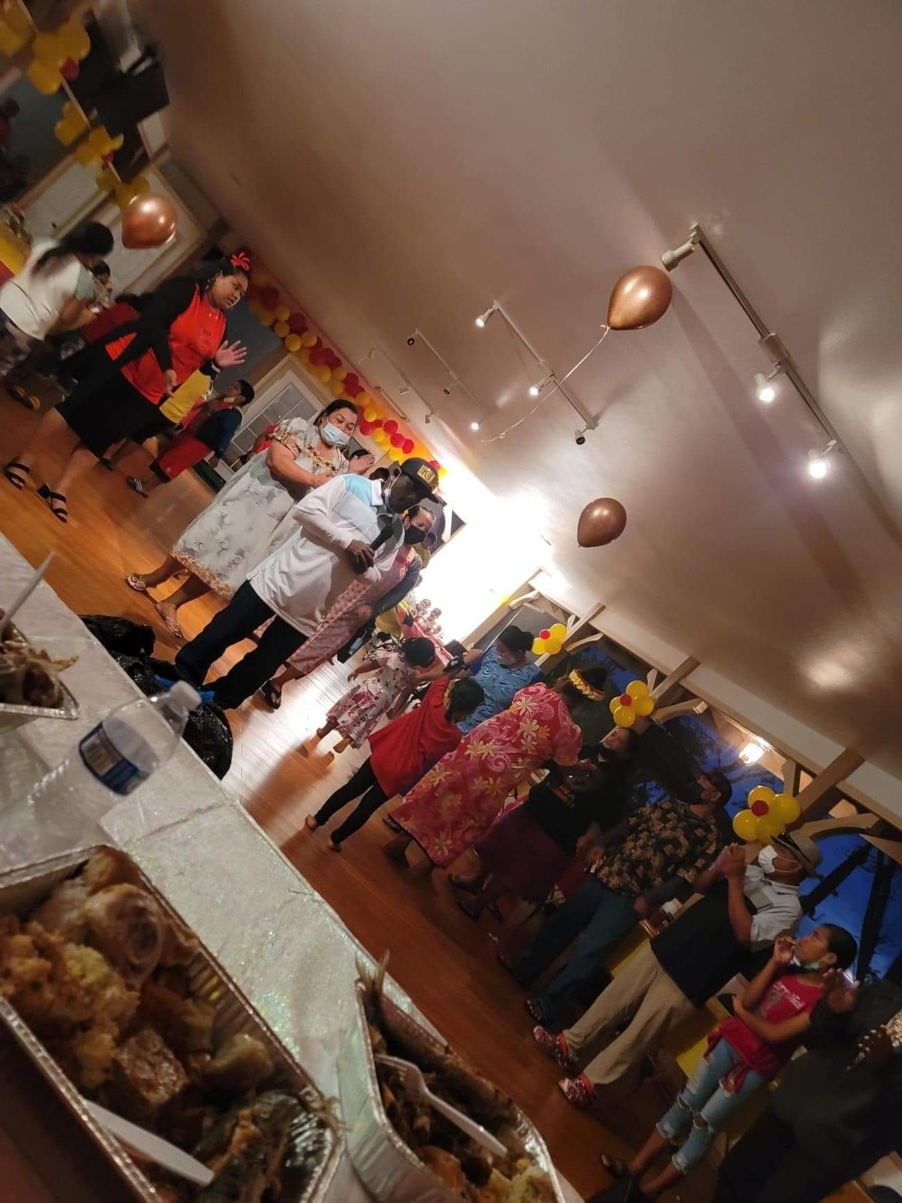 People at a party with balloons, food on a table, and warm lighting inside.